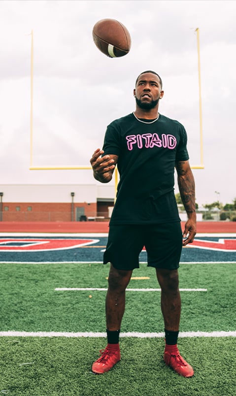 Brand ambassador on a football field, tossing a football, wearing a black FITAID shirt and black shorts